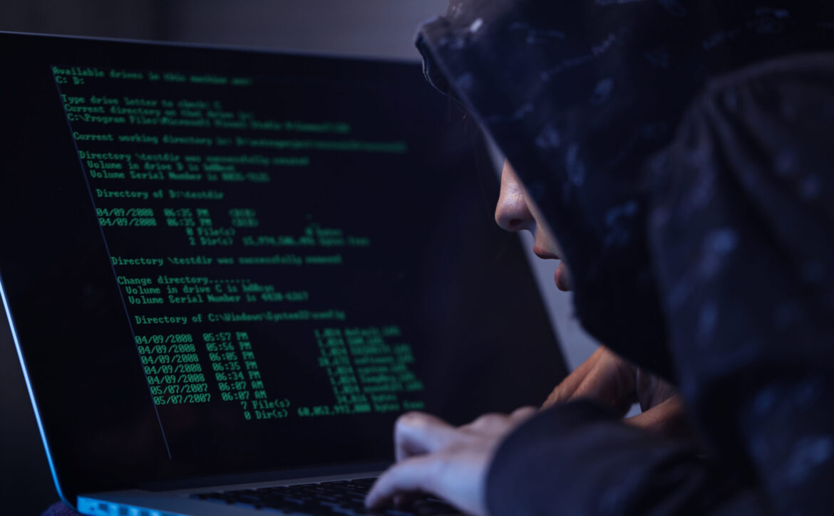 Computer hacker programming software while stealing data on laptop.